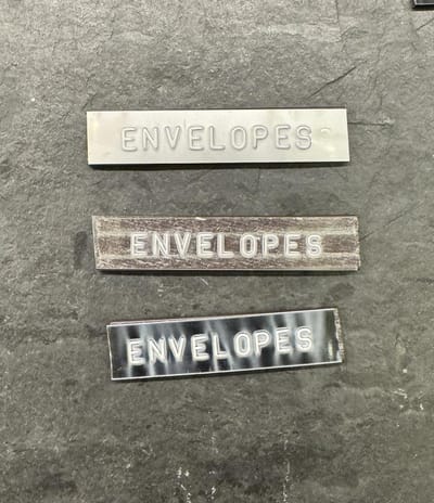 Three embossed labels reading ENVELOPES on metal, clear and black tape, laid on dark slate